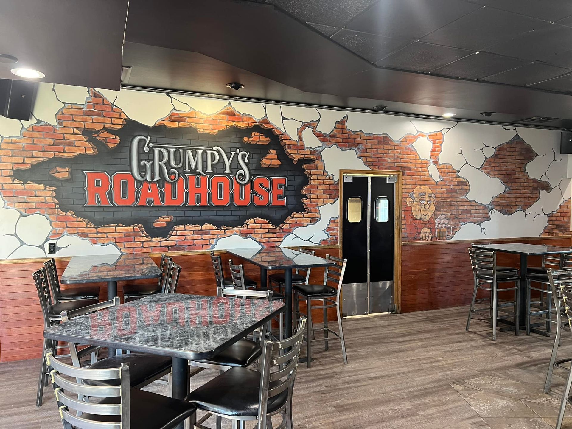 A restaurant with tables and chairs and a sign that says grumpy 's roadhouse.