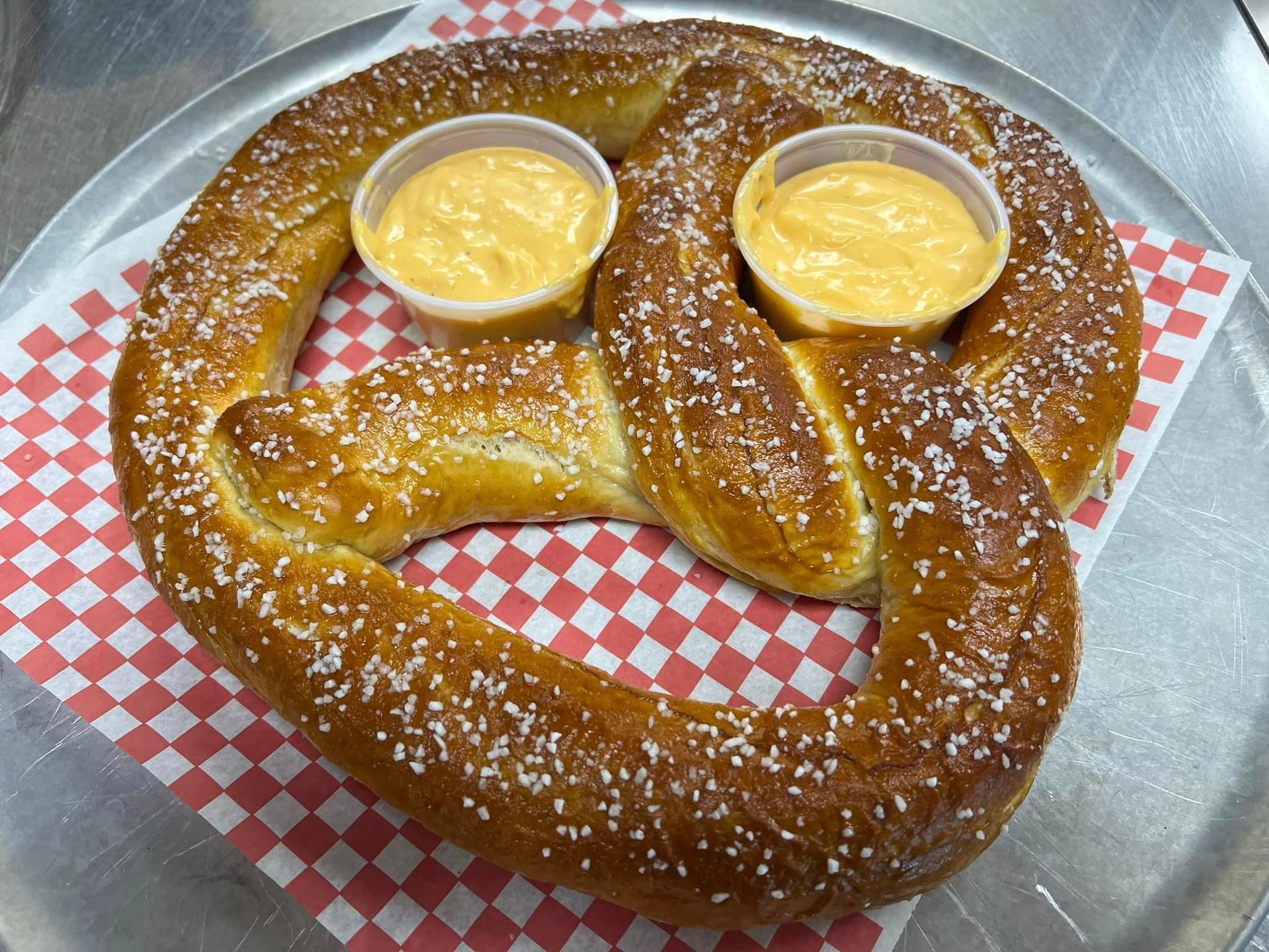 A pretzel shaped like a smiley face with two dipping sauces on it.