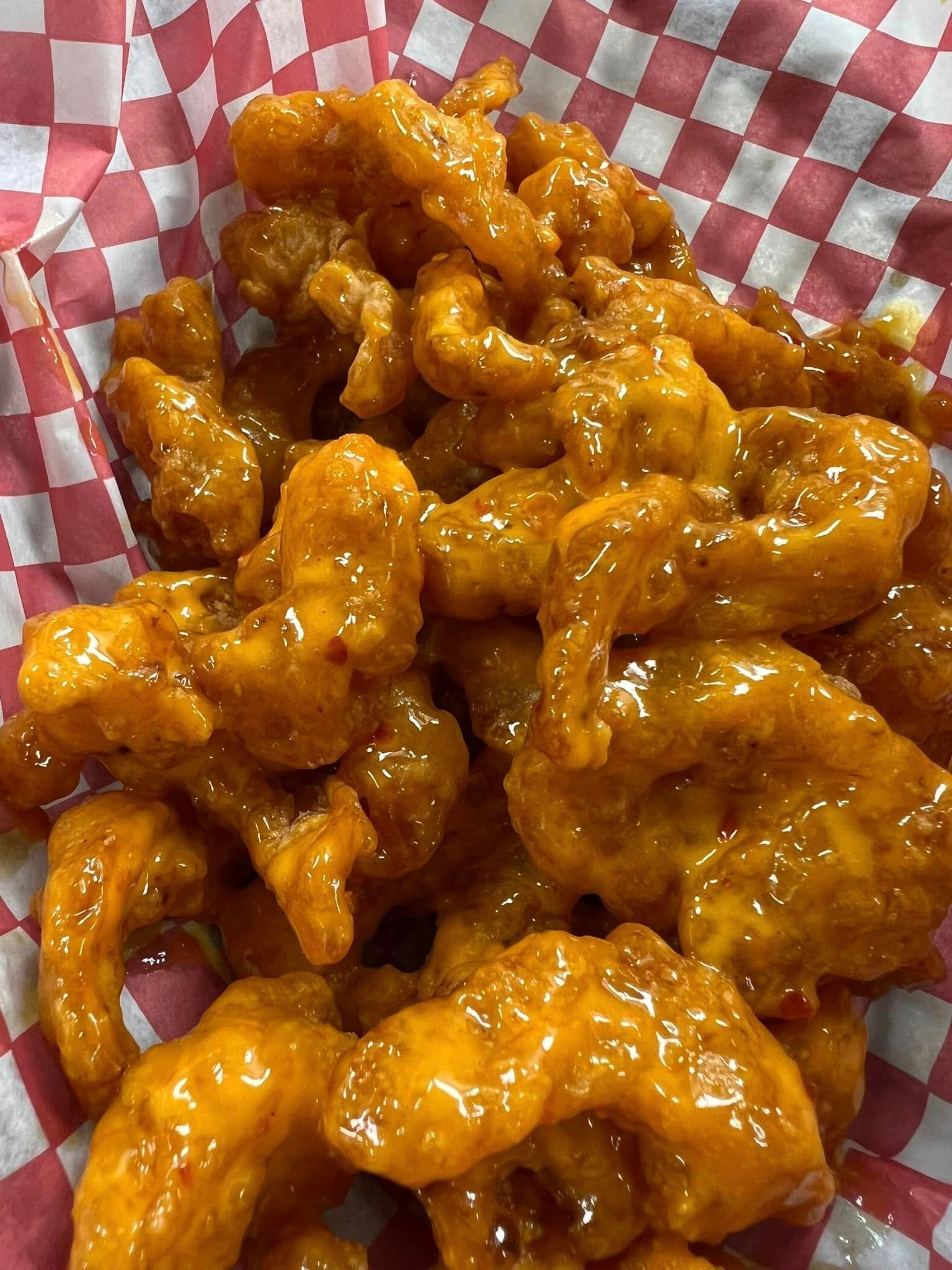 A close up of a basket of fried chicken on a checkered paper.