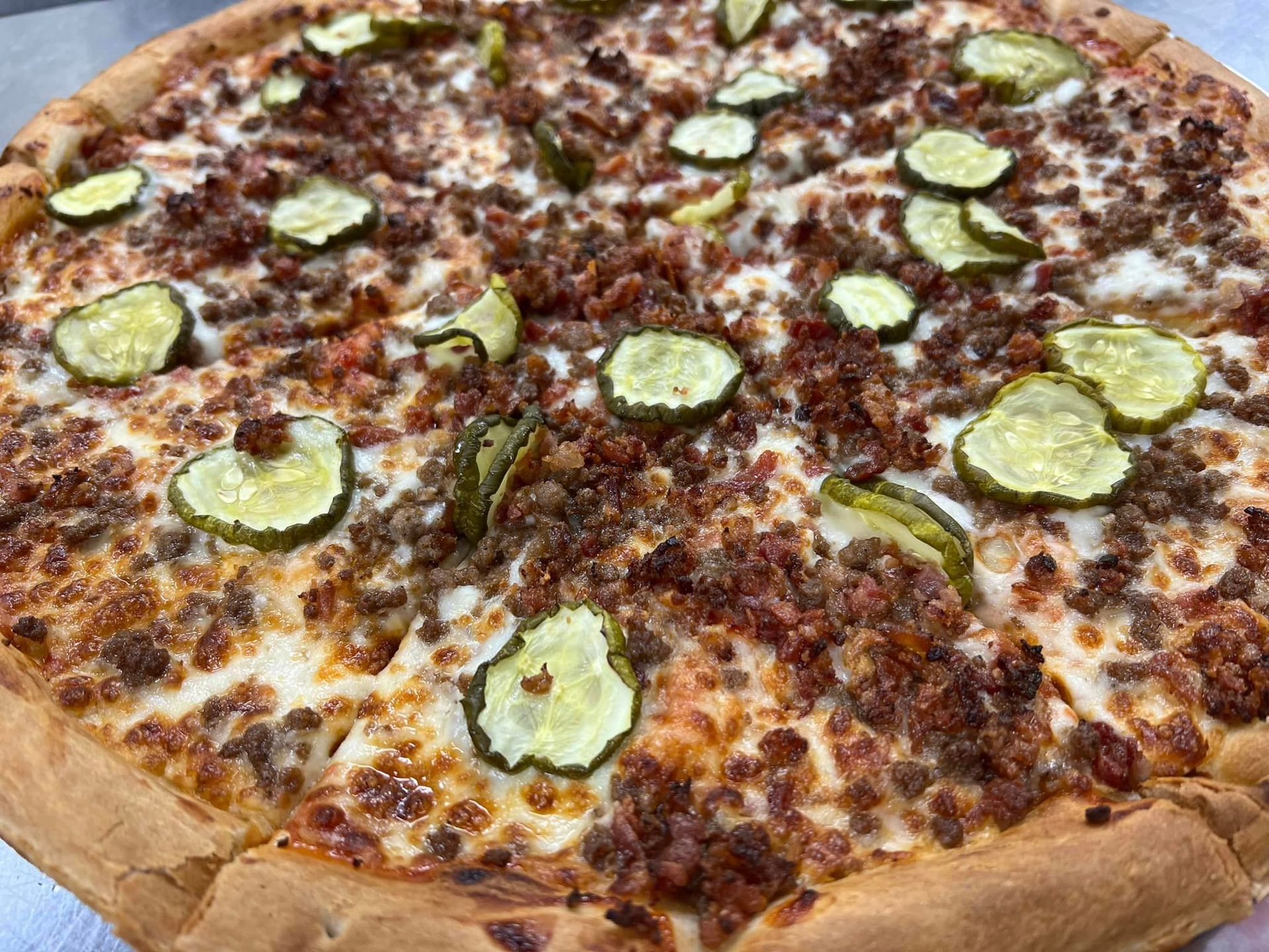 A pizza with meat and pickles on it is sitting on a table.