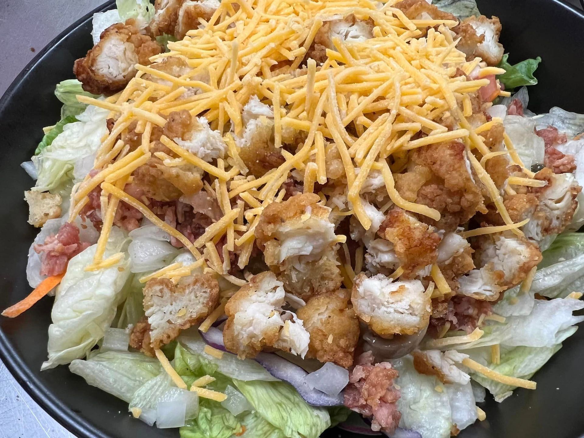 A salad with lettuce , chicken , cheese and croutons on a black plate.