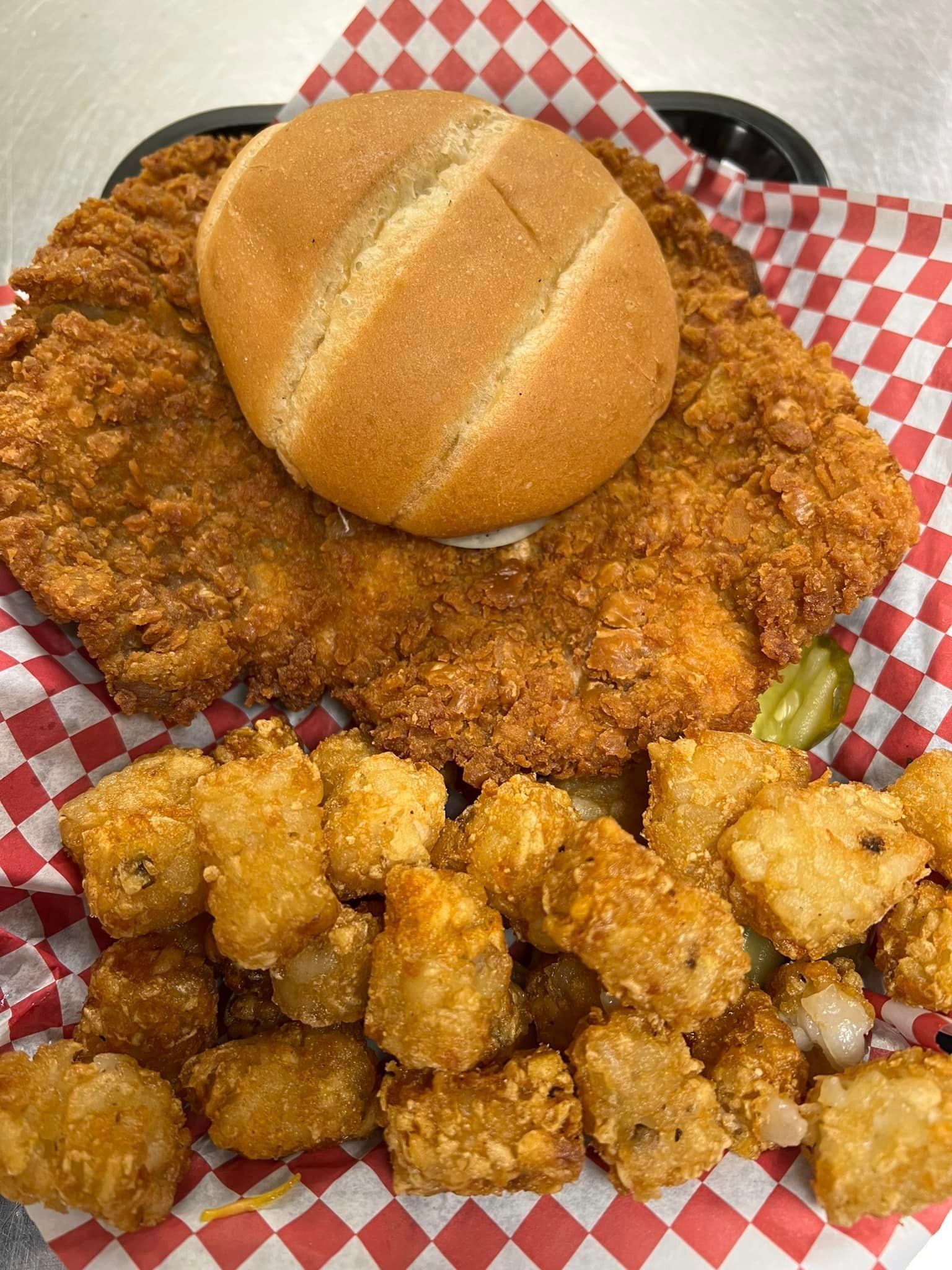 A fried chicken sandwich with a bun and tots on a checkered paper.
