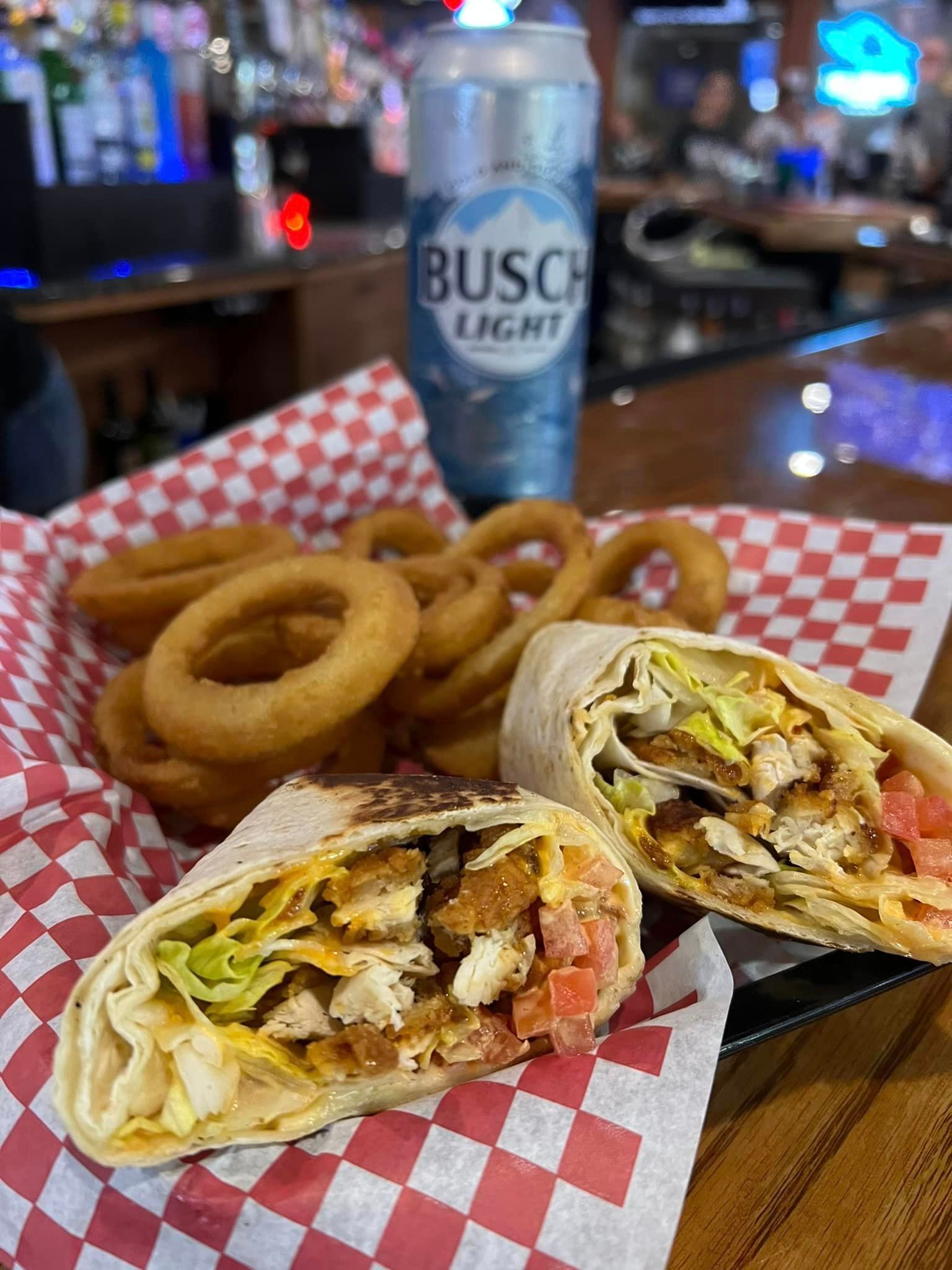 A wrap and onion rings are on a table next to a can of beer.
