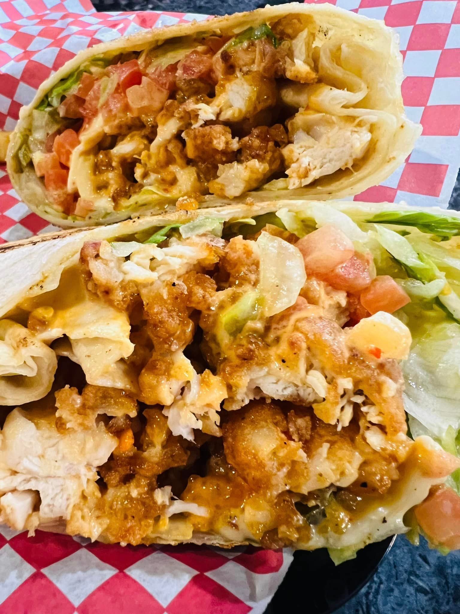 A burrito with chicken , lettuce , tomatoes and cheese is cut in half on a checkered paper.