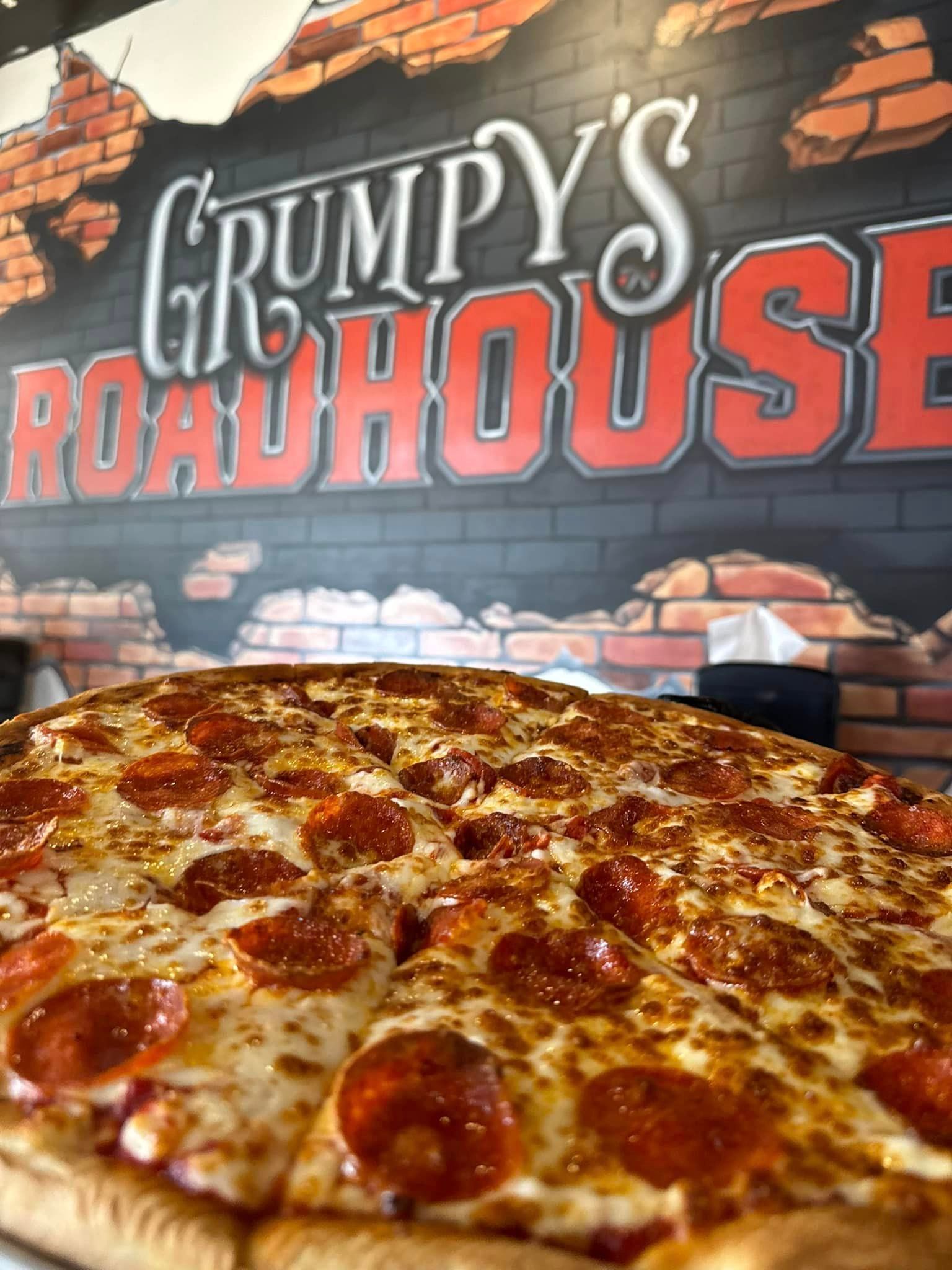 A pepperoni pizza is sitting on a table in front of a grumpy 's roadhouse sign.
