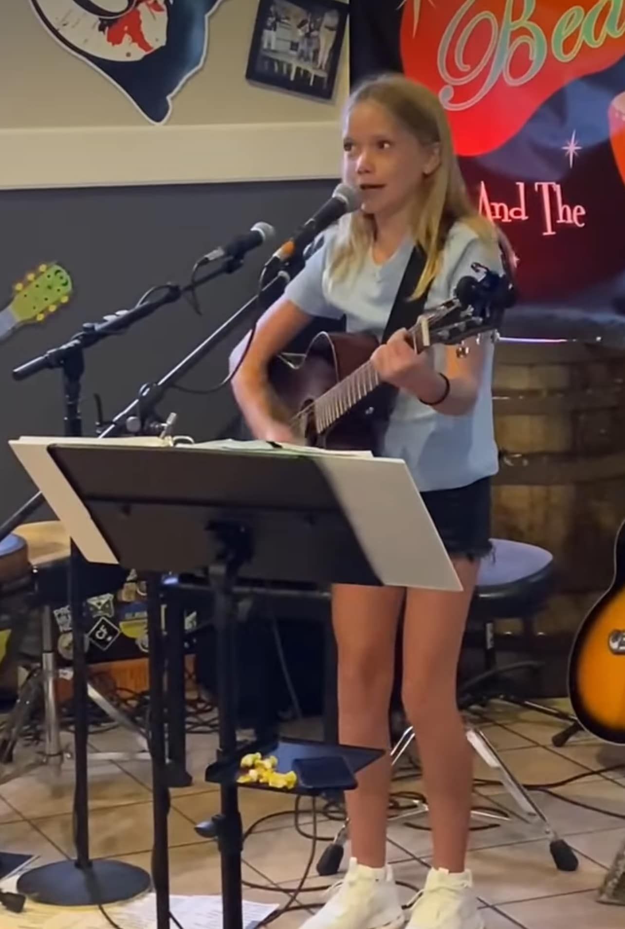 A young girl singing into a microphone while playing a guitar