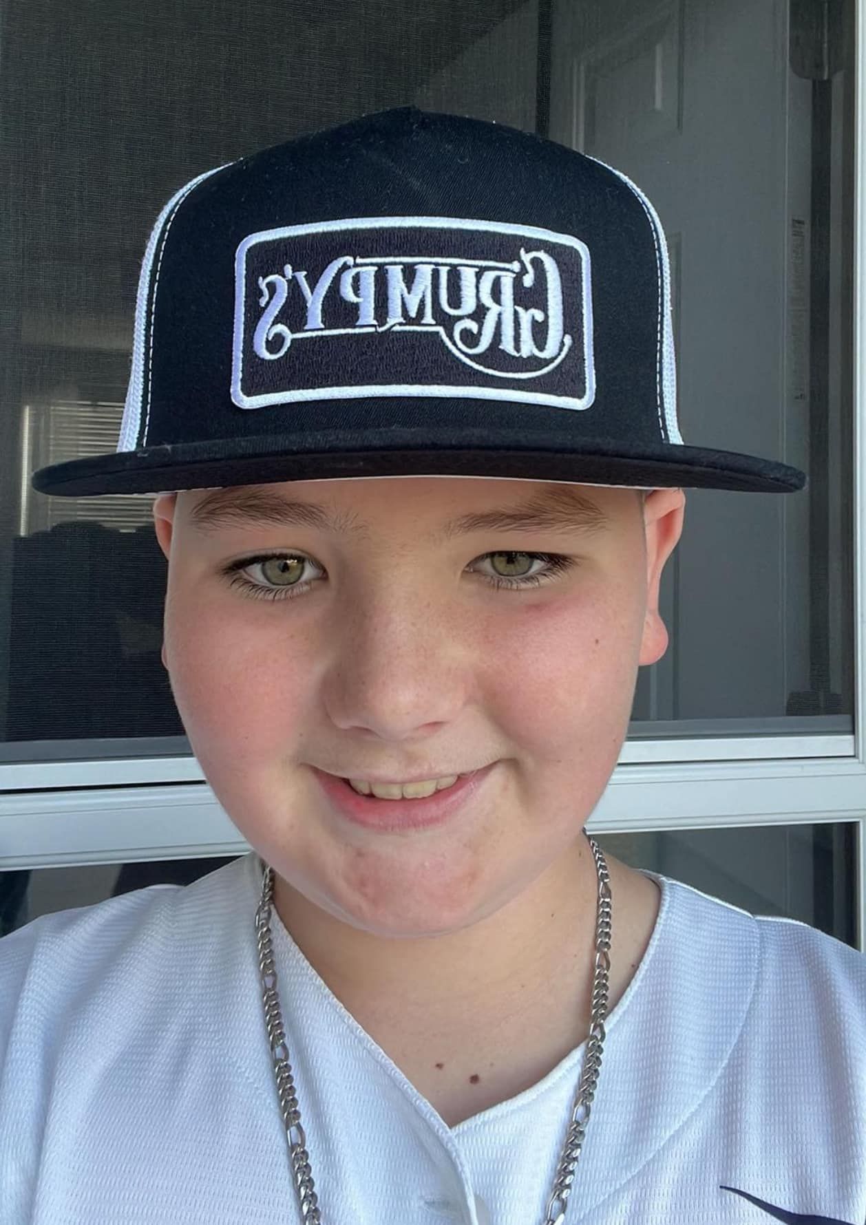 A young boy wearing a black hat and a white shirt is smiling.
