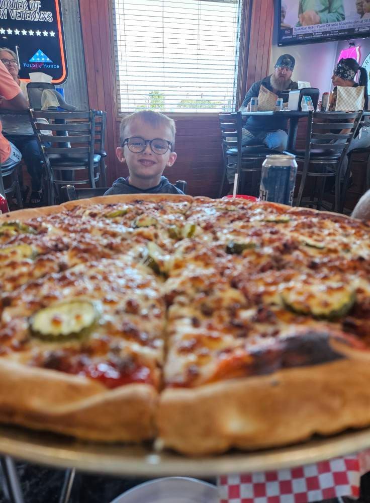 A young boy is sitting in front of a large pizza.