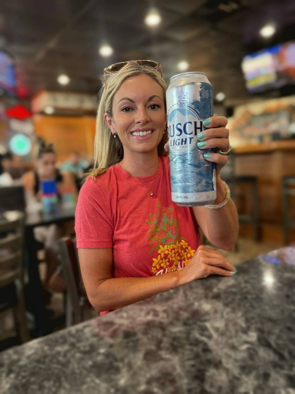 A woman is sitting at a table holding a can of beer.