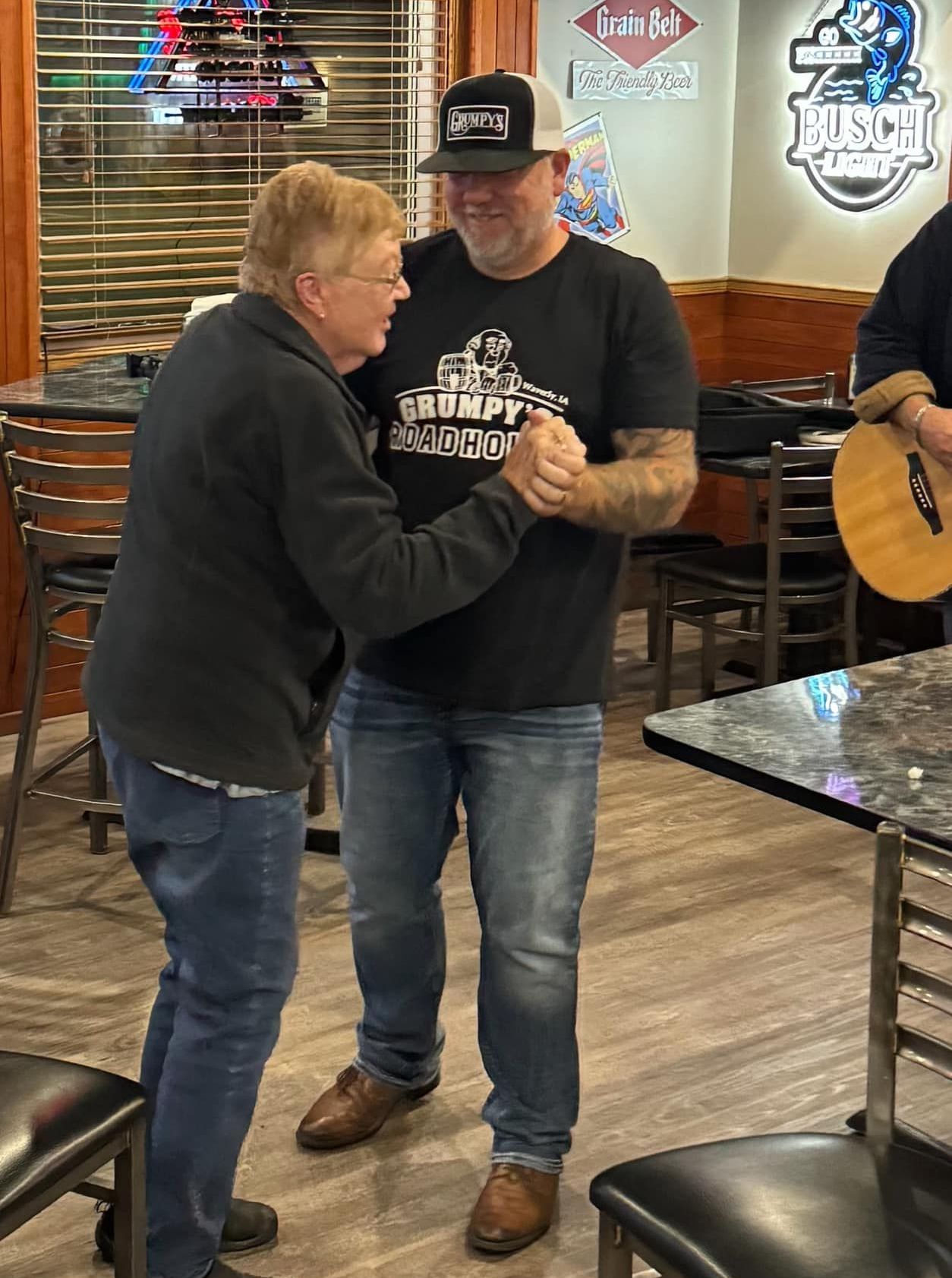 Two men are dancing in a restaurant while a man plays a guitar.