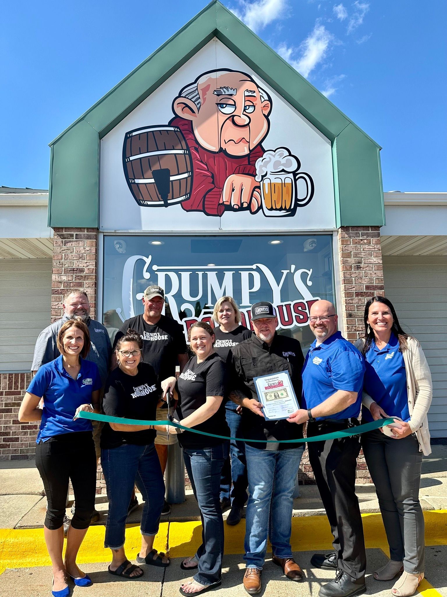 A group of people are standing in front of a building holding a green ribbon.