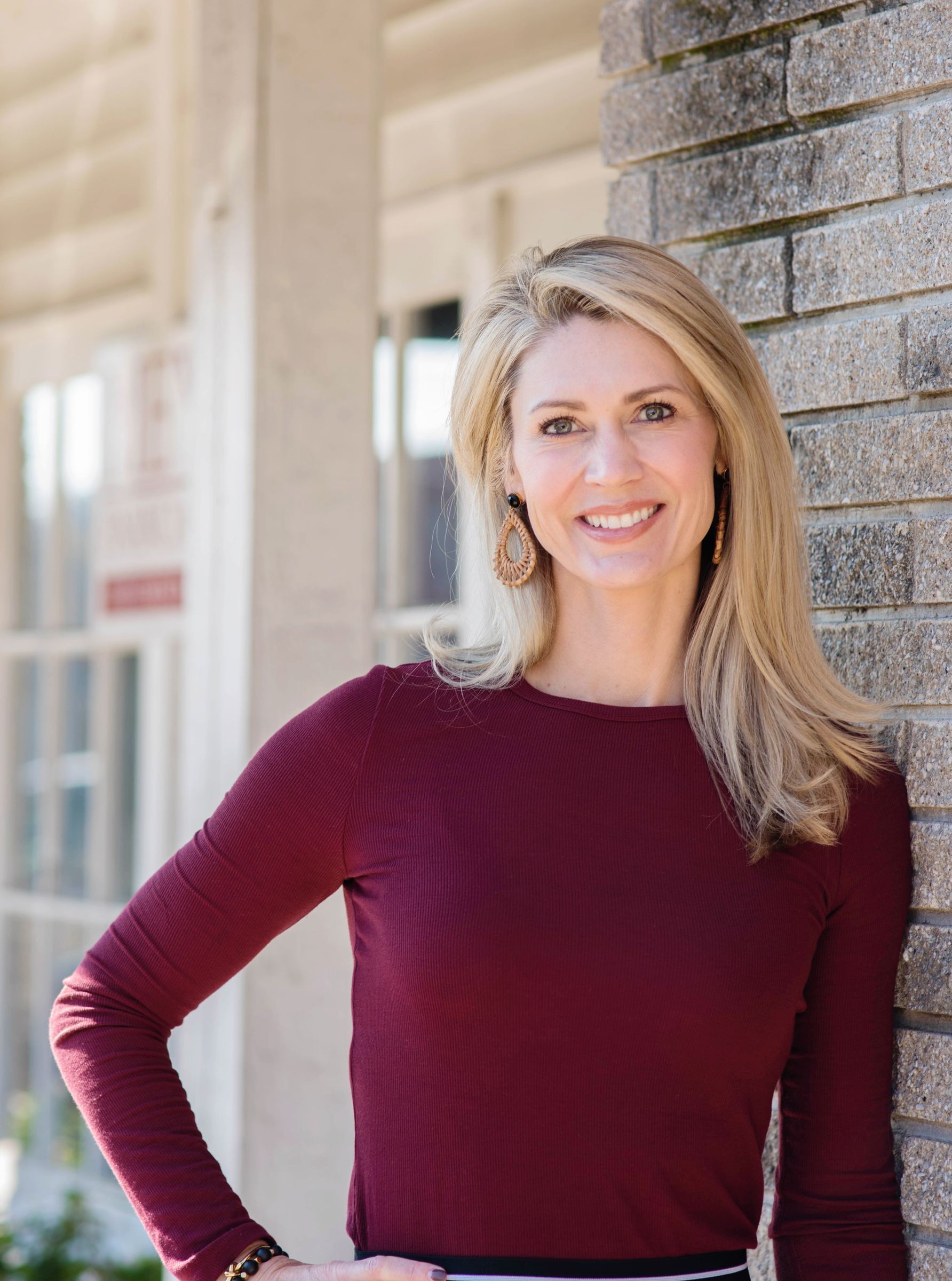 A woman in a red sweater is leaning against a brick wall and smiling.