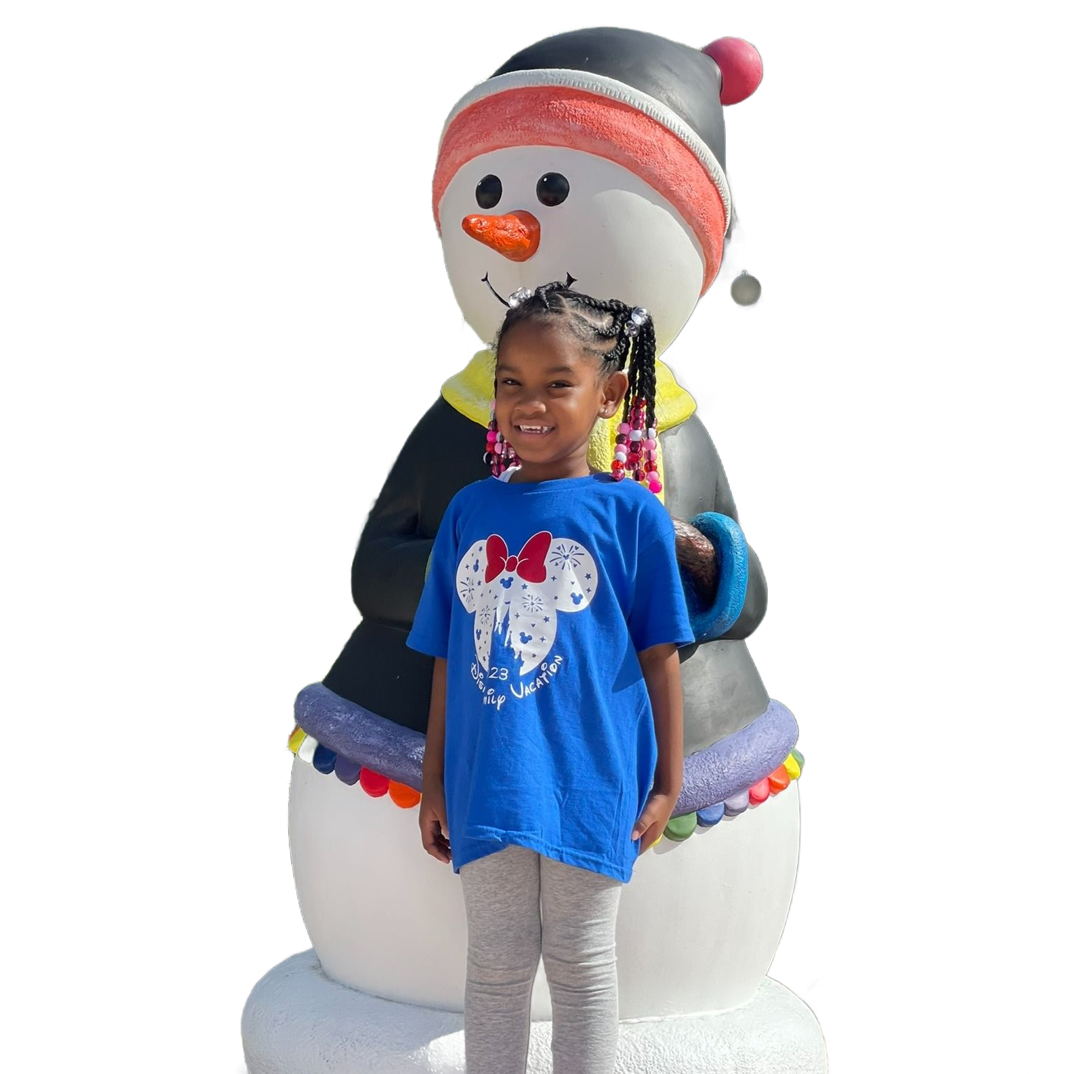 A smiling child wearing a blue Minnie Mouse t-shirt stands in front of a large, decorative snowman figure.