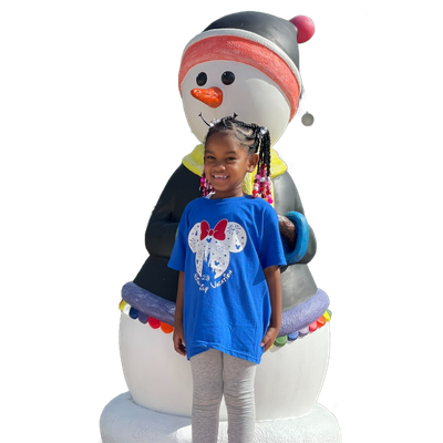 A smiling child wearing a blue Minnie Mouse t-shirt stands in front of a large, decorative snowman figure.