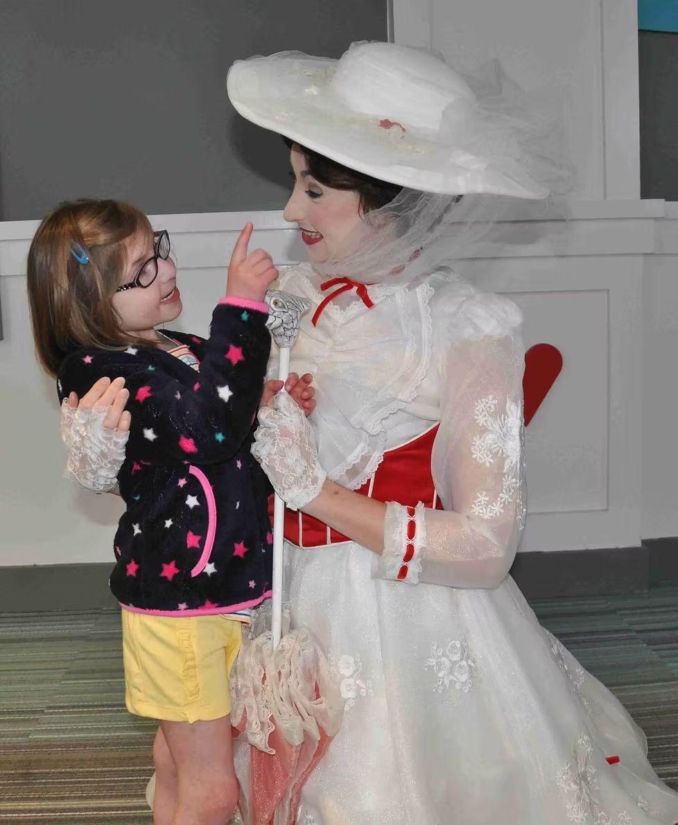 A child wearing glasses and a star-patterned jacket points a finger at a performer dressed as Mary Poppins.