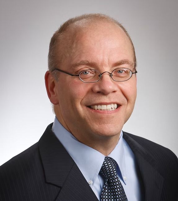 Young woman with brown hair laughs, wearing a green shirt, set against a white backdrop.