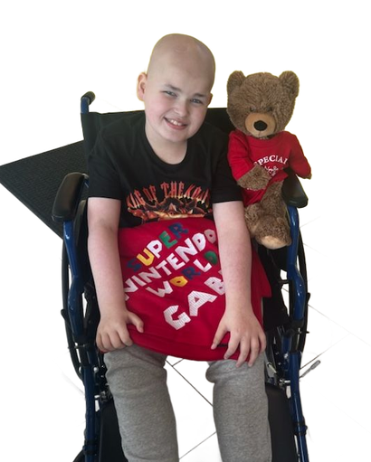 A smiling person sits in a wheelchair holding a teddy bear with a red shirt, wearing a black shirt and grey pants.
