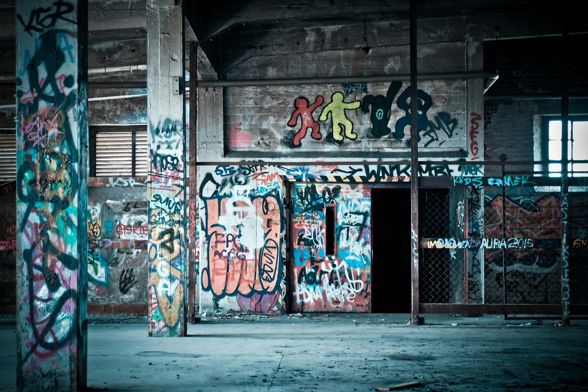 An interior of an abandoned building covered in colorful graffiti art. A doorway and pillars are prominent features.
