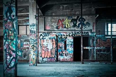 An interior of an abandoned building covered in colorful graffiti art. A doorway and pillars are prominent features.