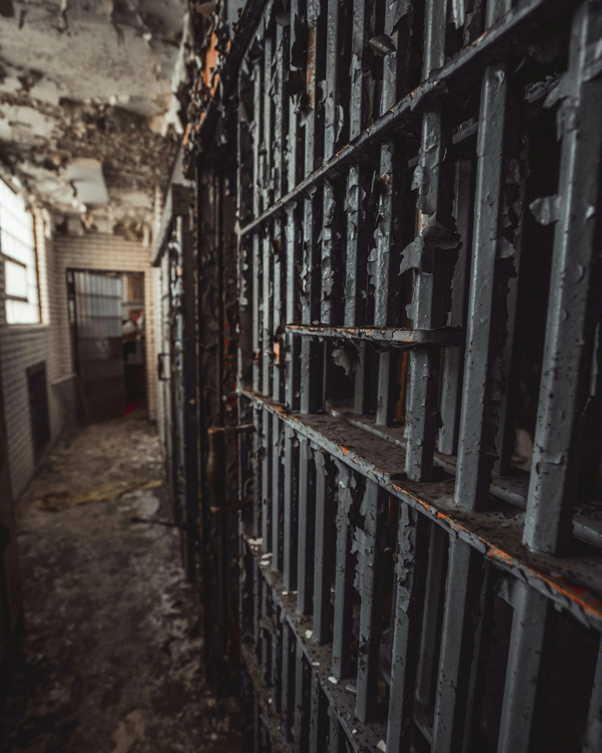 An old prison hallway with rusted, dark bars. Peeling paint and decay evident, hinting at abandonment.