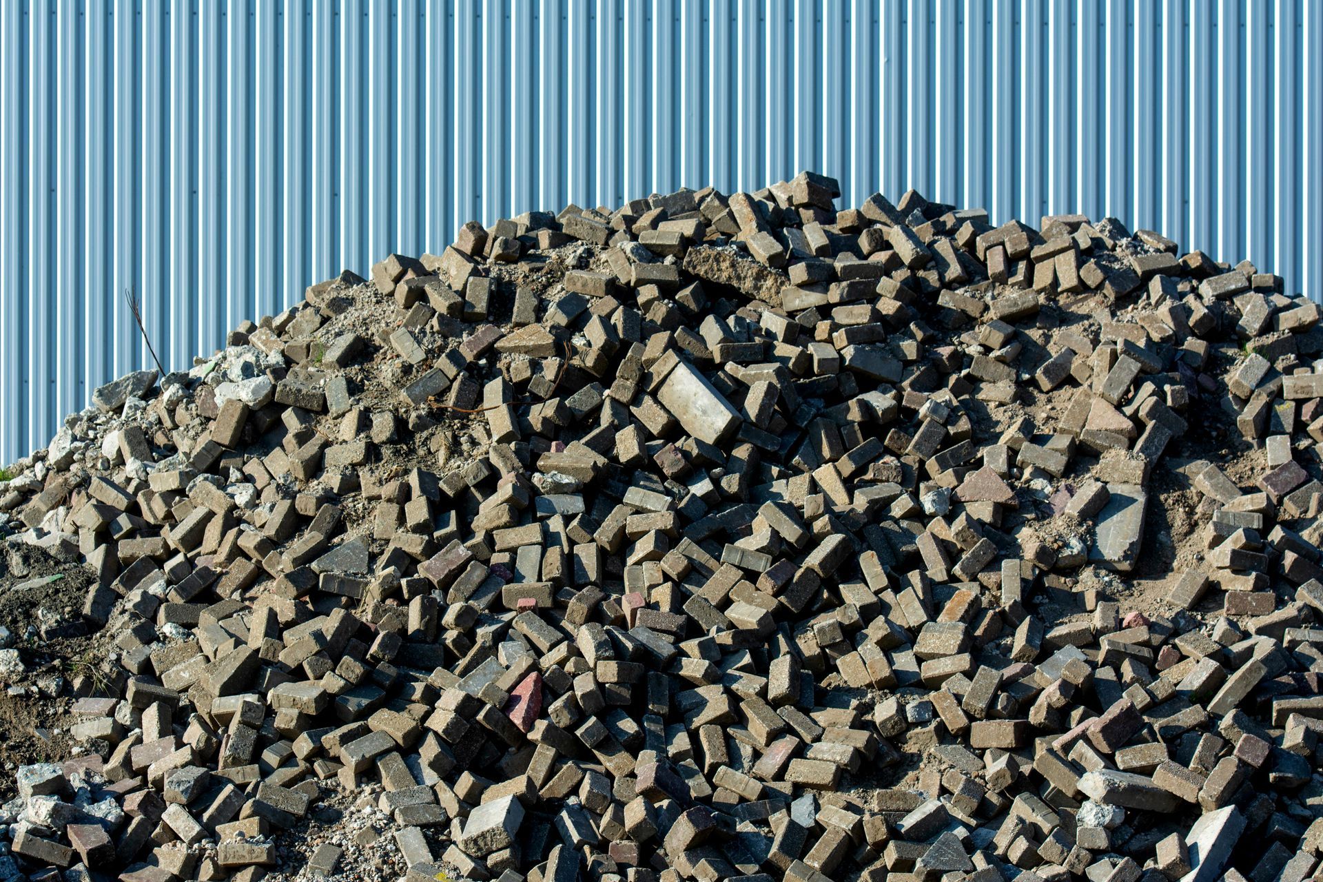 Pile of broken bricks against a corrugated metal wall.