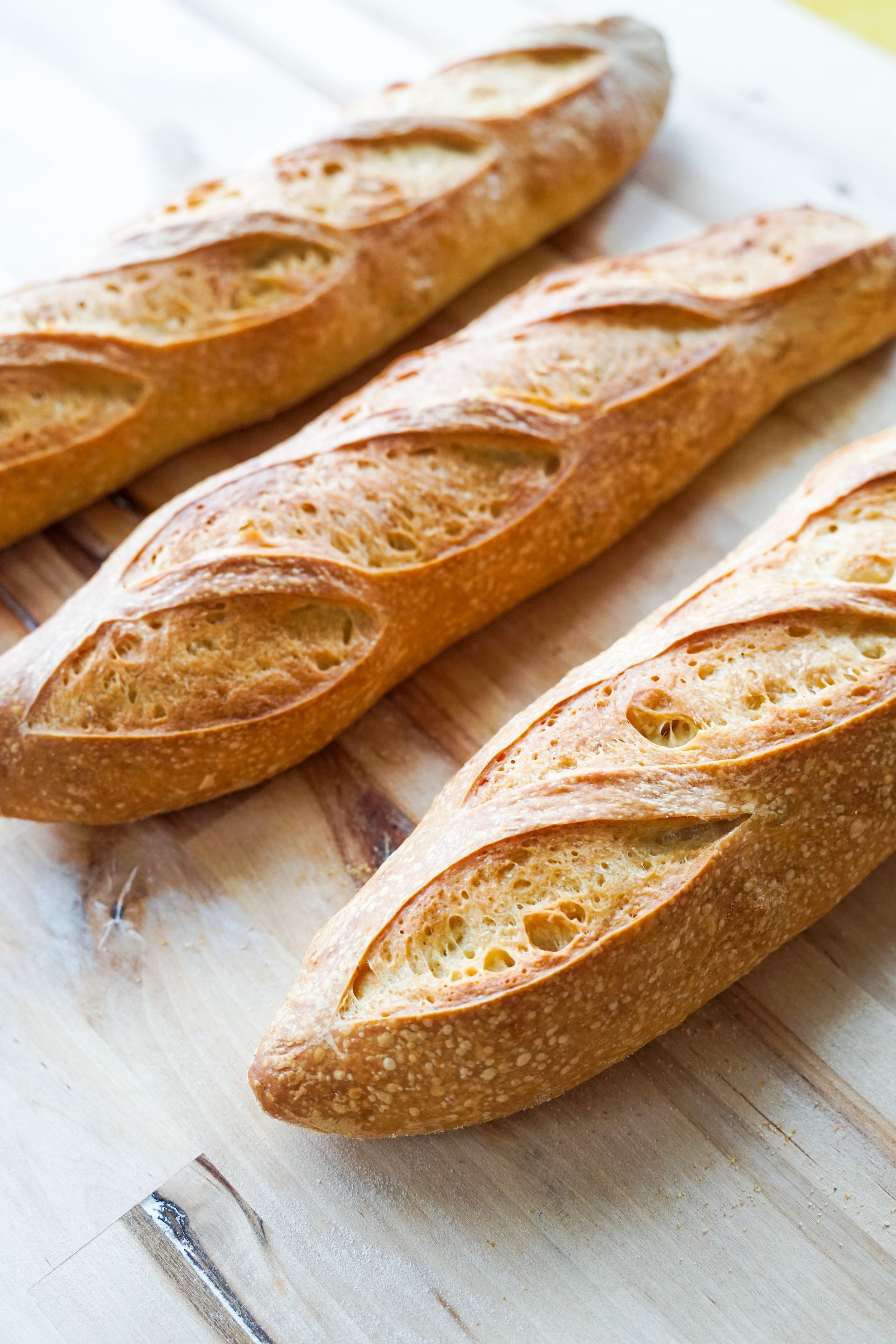 Three baguettes are sitting on a wooden cutting board.
