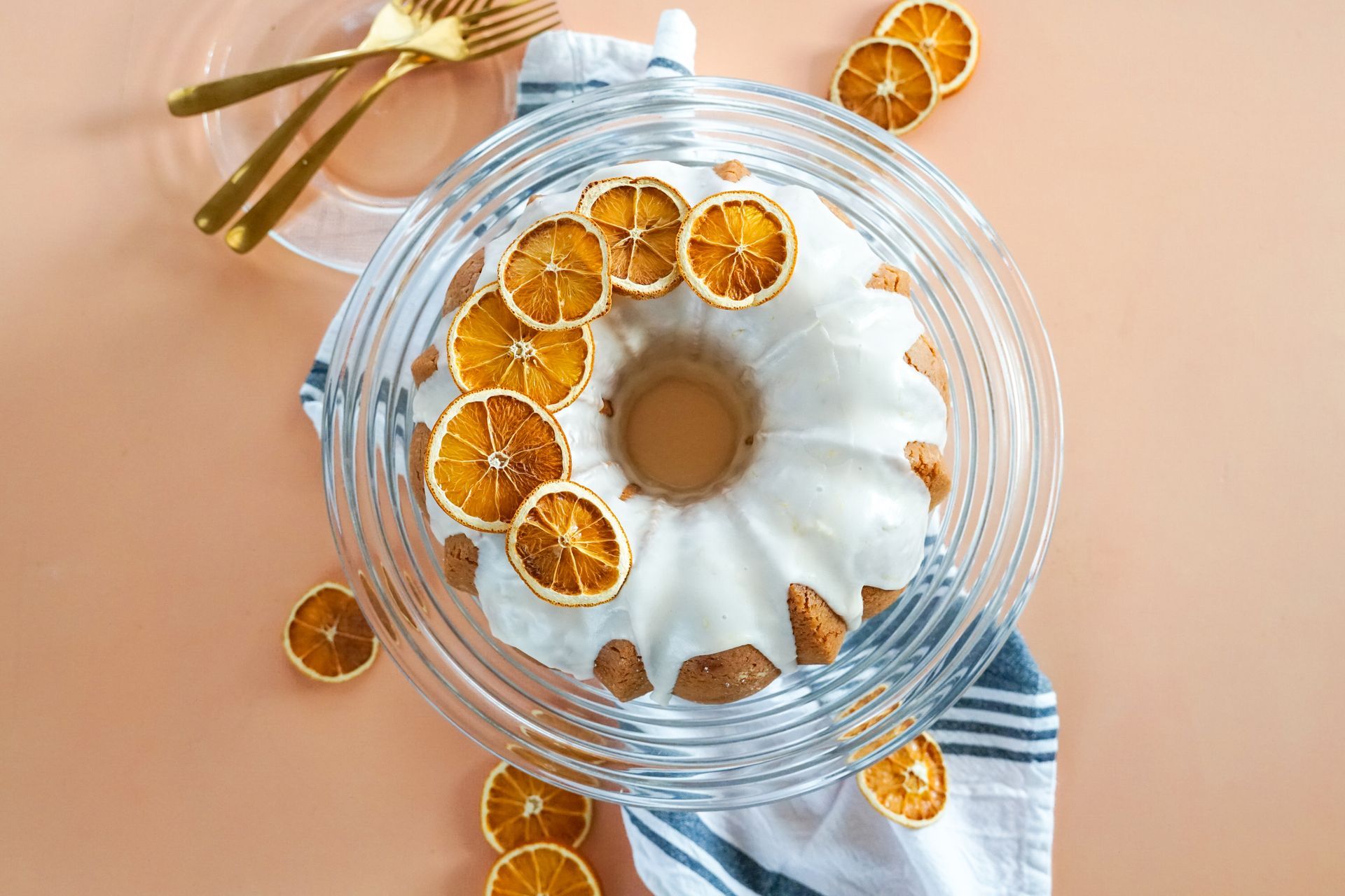 A bundt cake with icing and dried oranges on a glass plate.