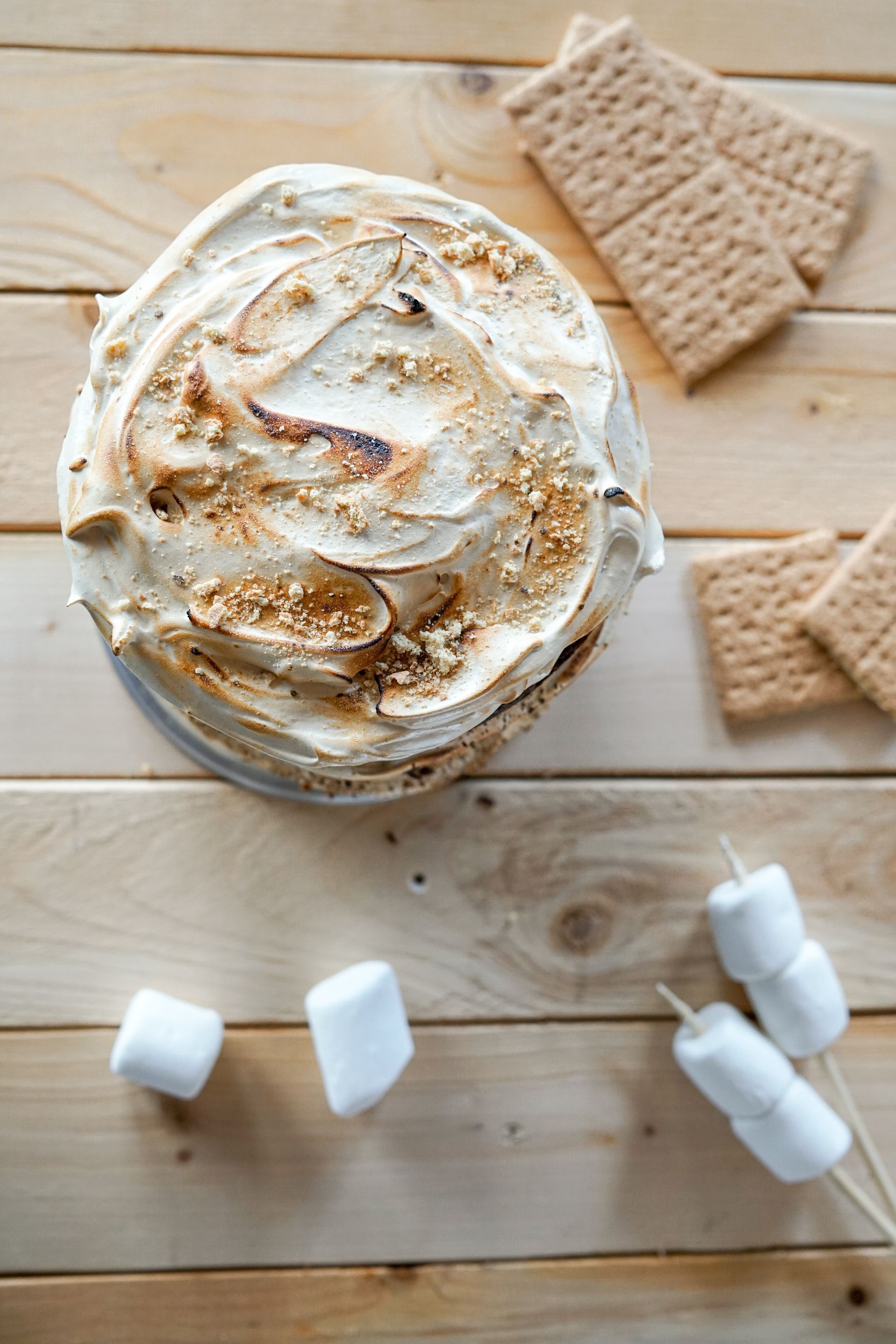 A s'mores cake with marshmallows and graham crackers on a wooden table.