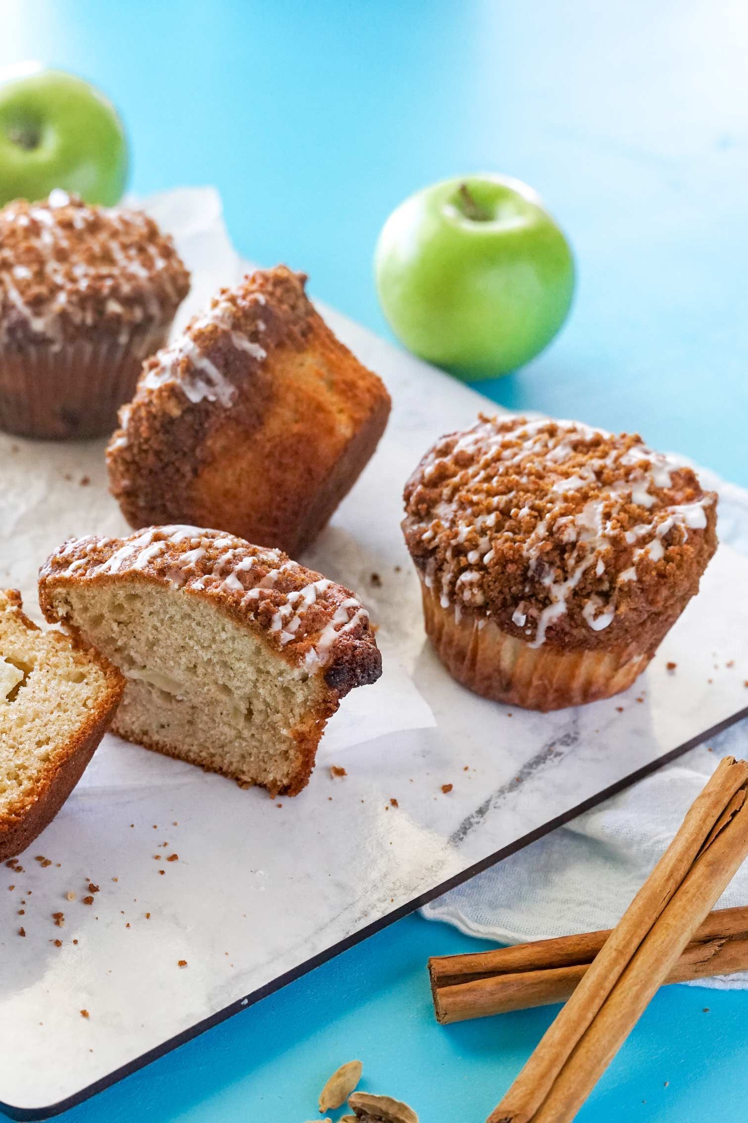 A tray of muffins with cinnamon sticks and apples on a table.