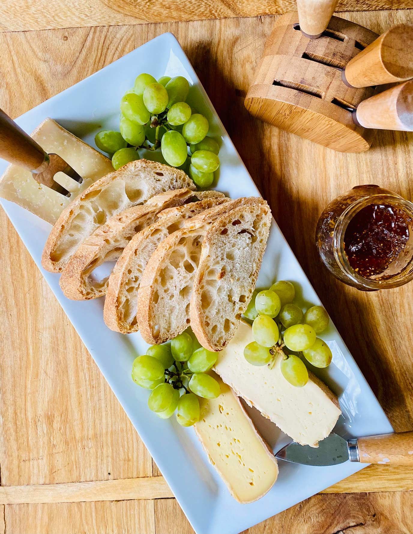 A white plate topped with cheese , bread and grapes on a wooden table.