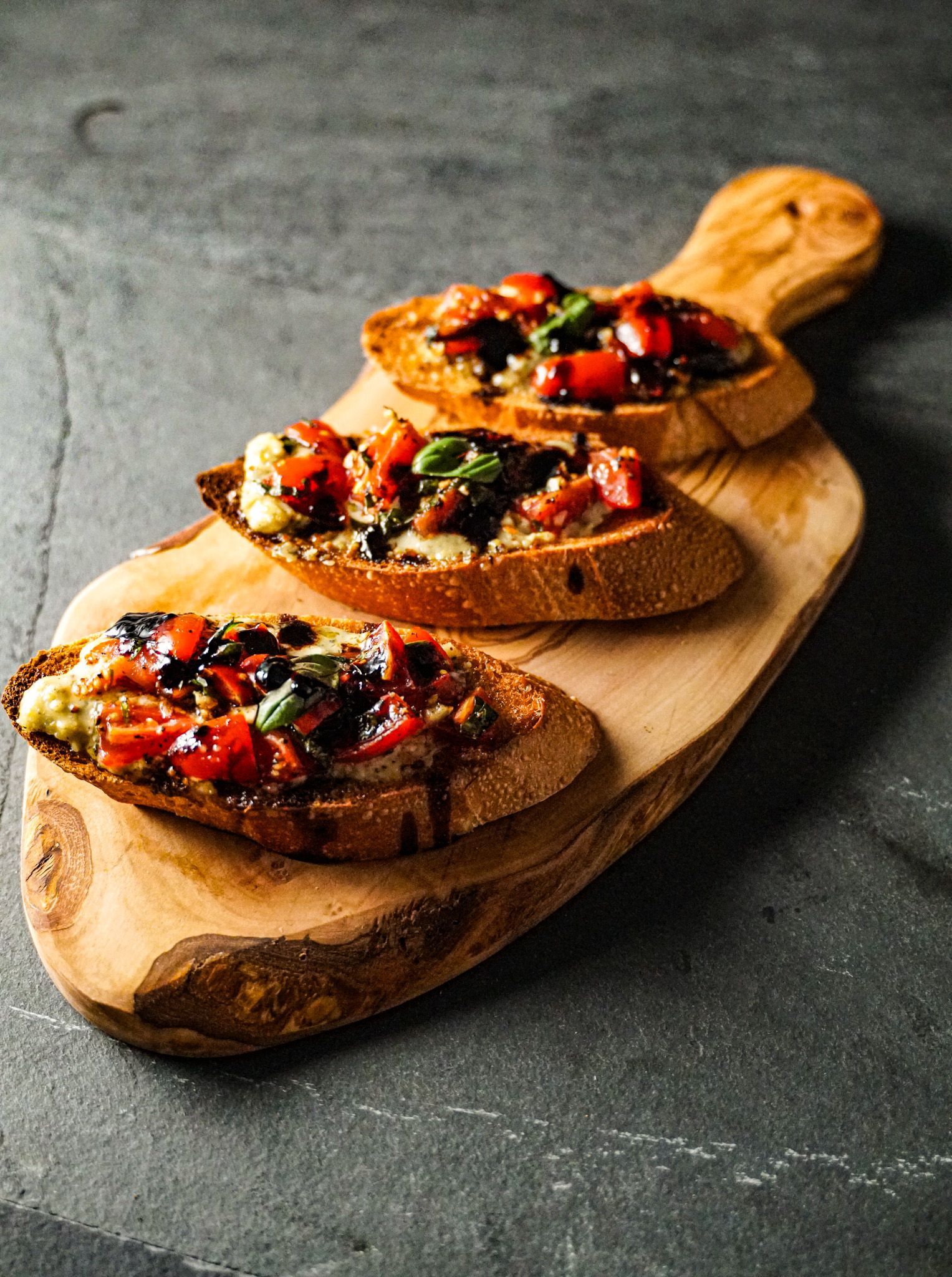 Three slices of bread with vegetables on a wooden cutting board.