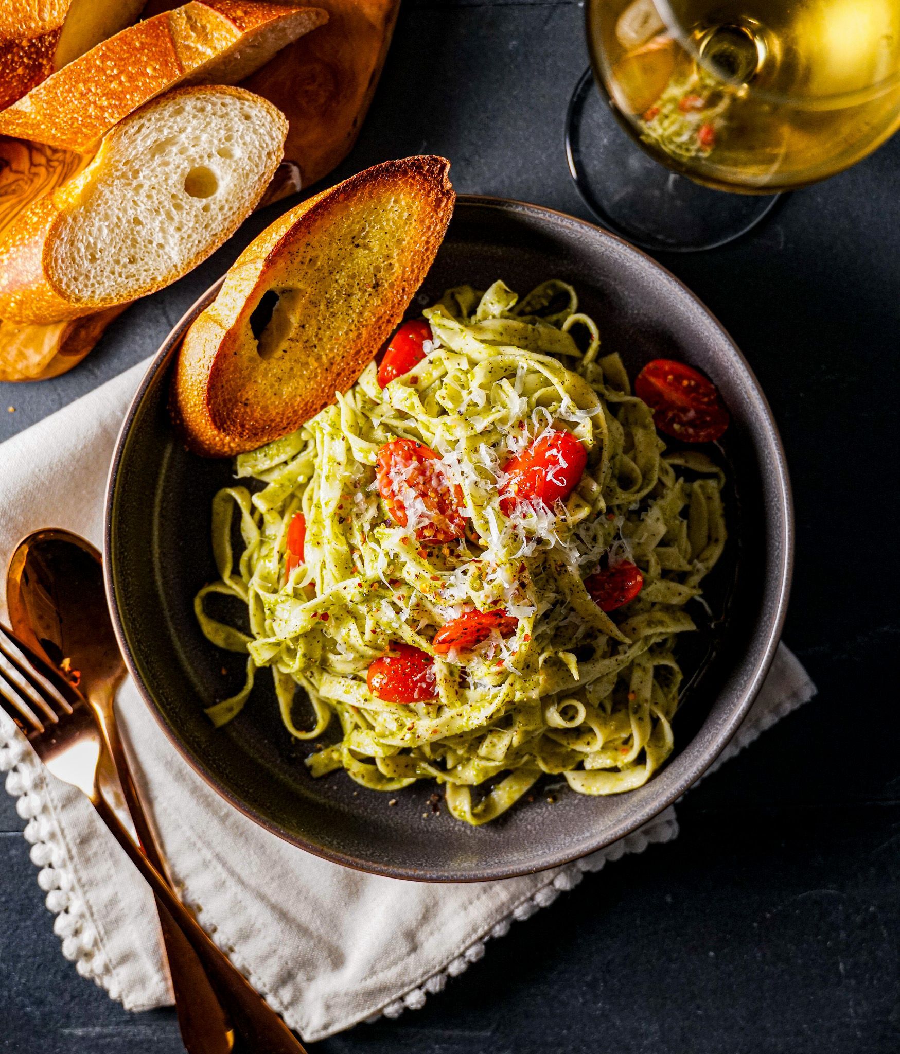 A bowl of pasta with tomatoes and garlic bread next to a glass of wine.