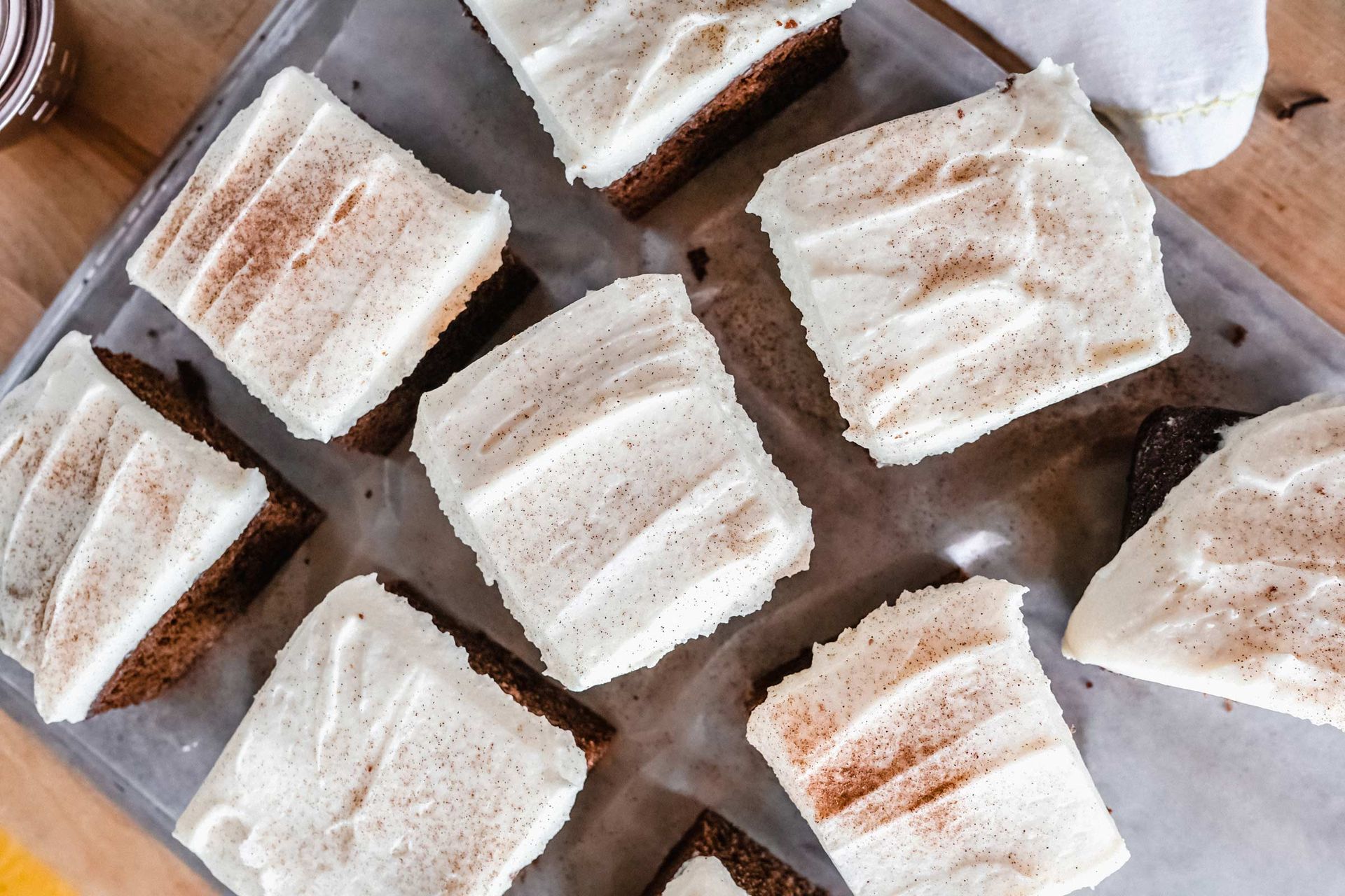 A tray of brownies with white frosting on a wooden table.
