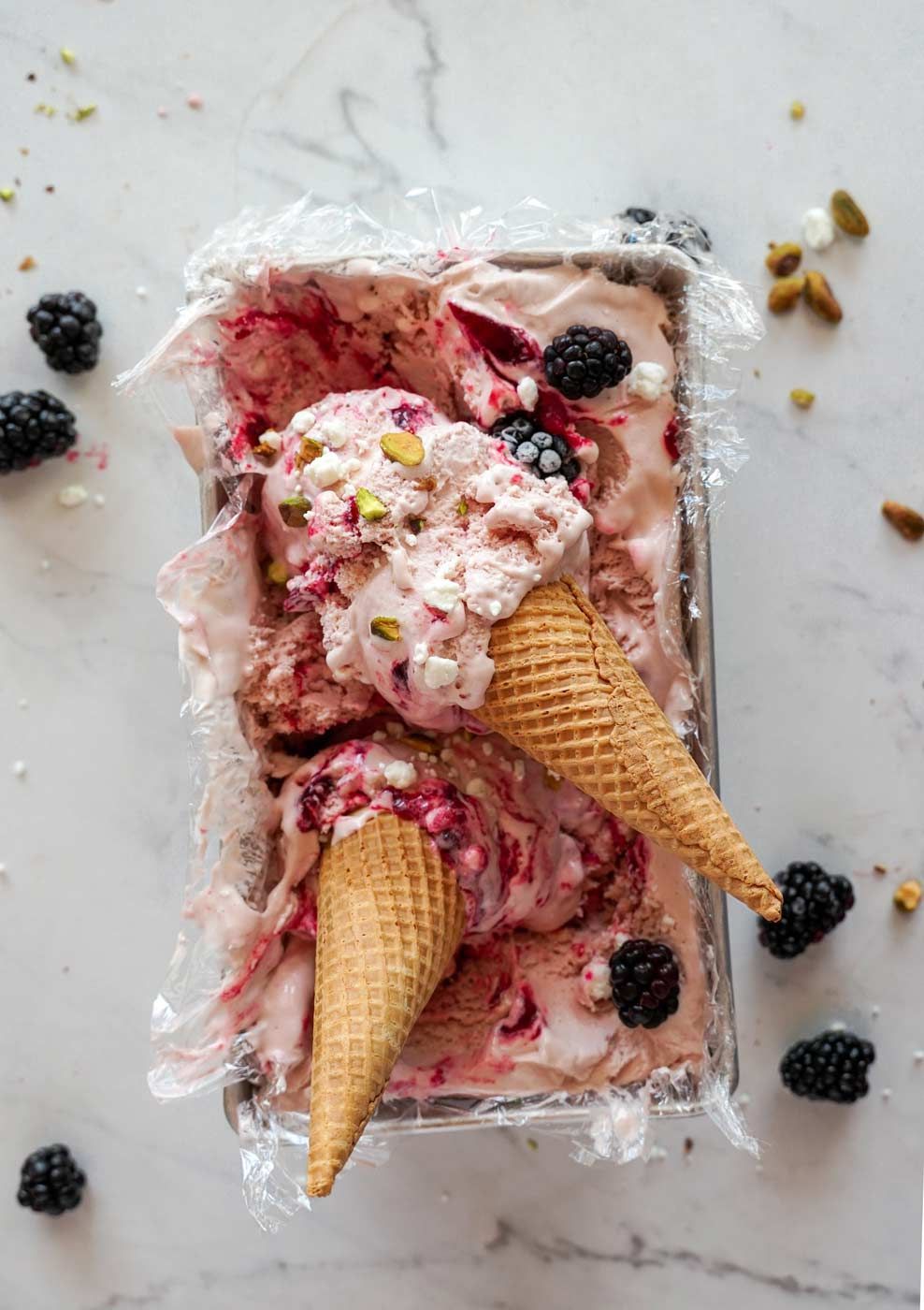 Two ice cream cones are sitting on top of a container of ice cream.