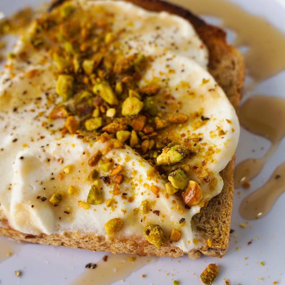 A close up of a piece of toast with ice cream and pistachios on a plate.