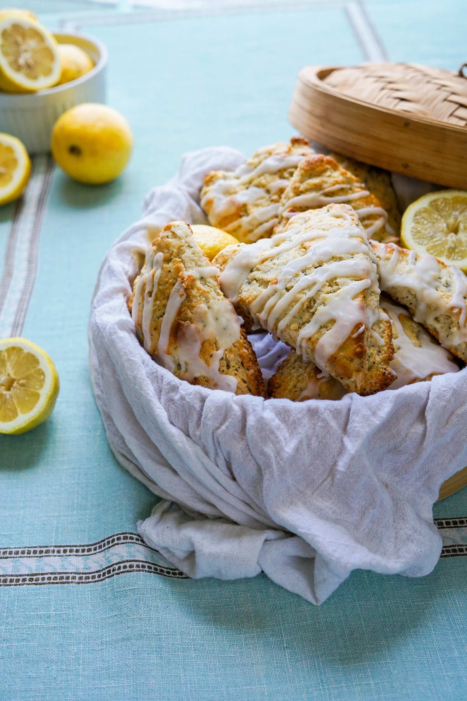 A basket filled with lemon scones and lemons on a table.