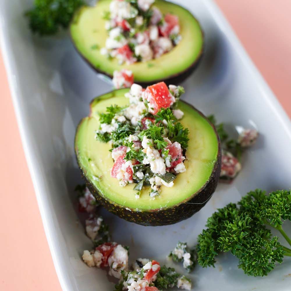 A white plate topped with avocado halves filled with vegetables.
