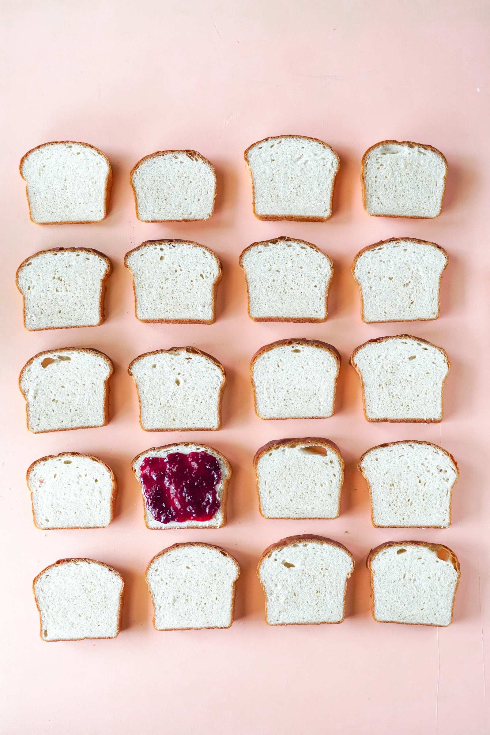 A bunch of slices of bread with jam on them on a pink surface.