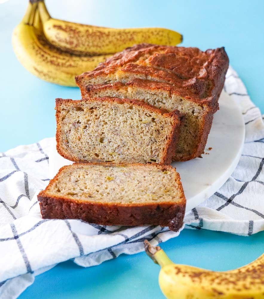 A loaf of banana bread is sitting on a white plate next to two bananas.