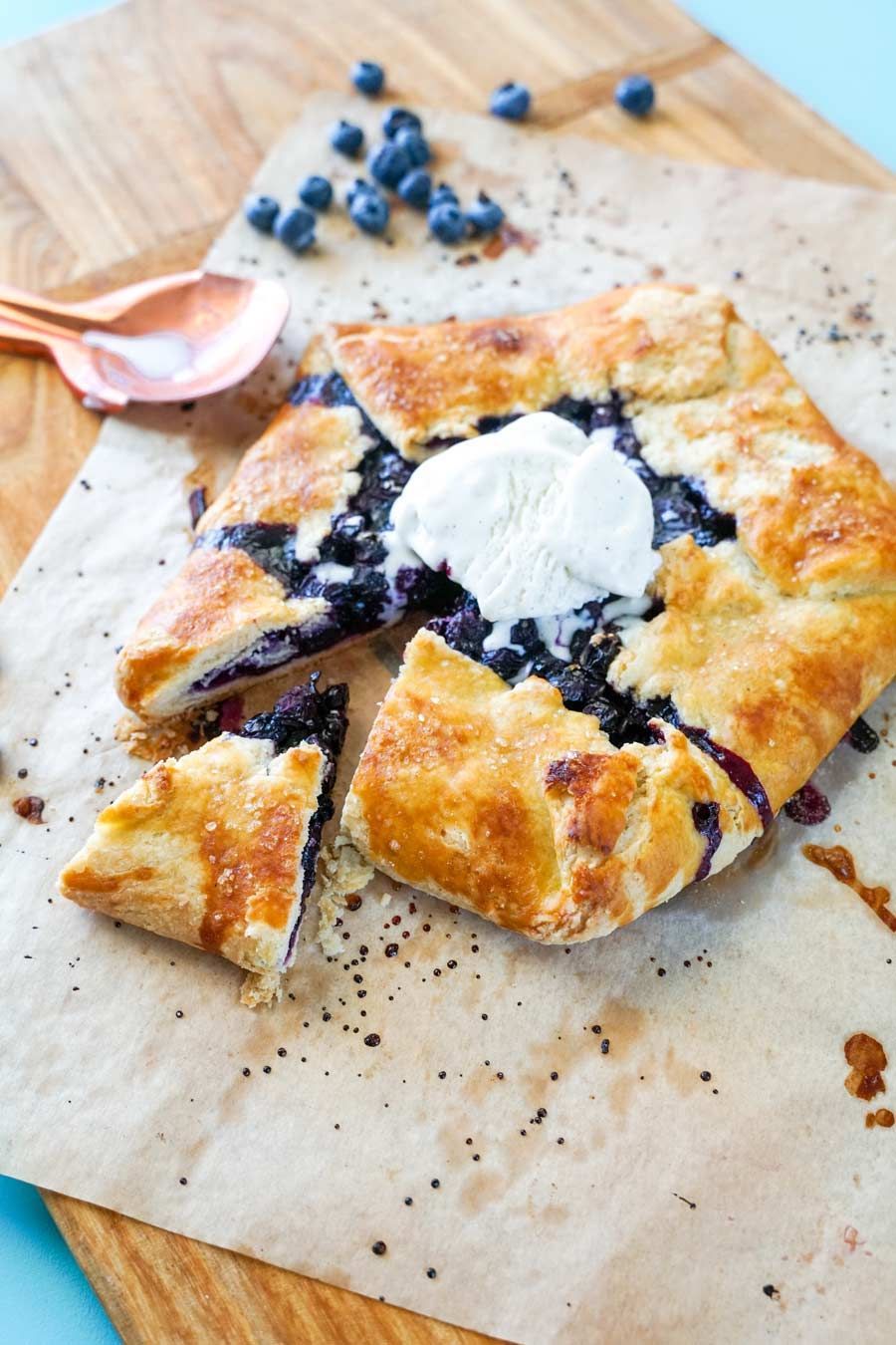 A blueberry pie with ice cream on top is sitting on a wooden cutting board.
