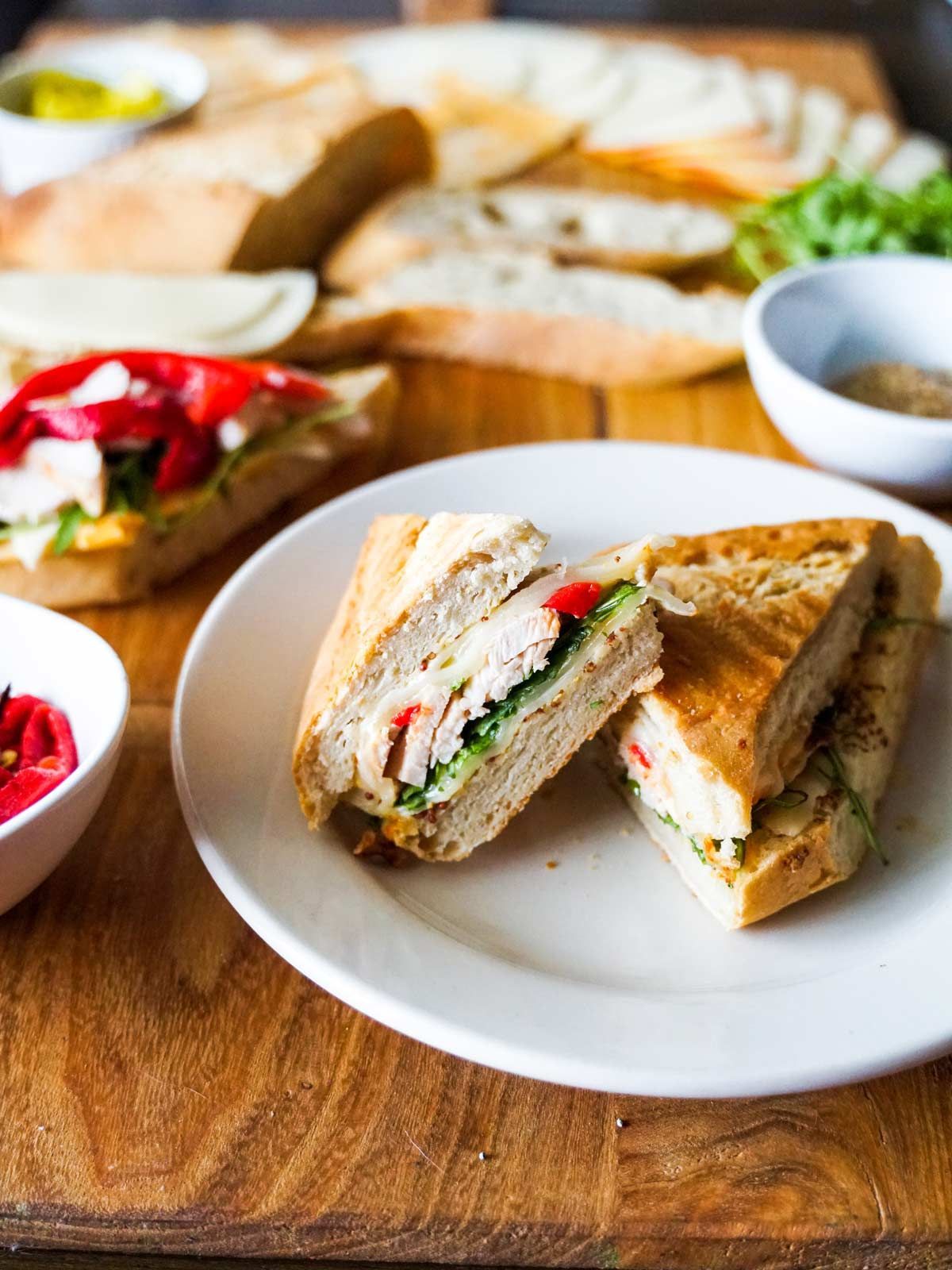 A sandwich is cut in half on a white plate on a wooden table.