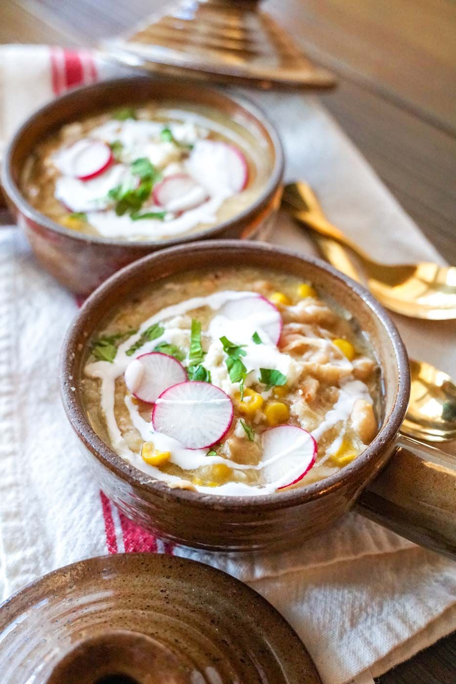 Two bowls of soup with radishes and sour cream on a table.