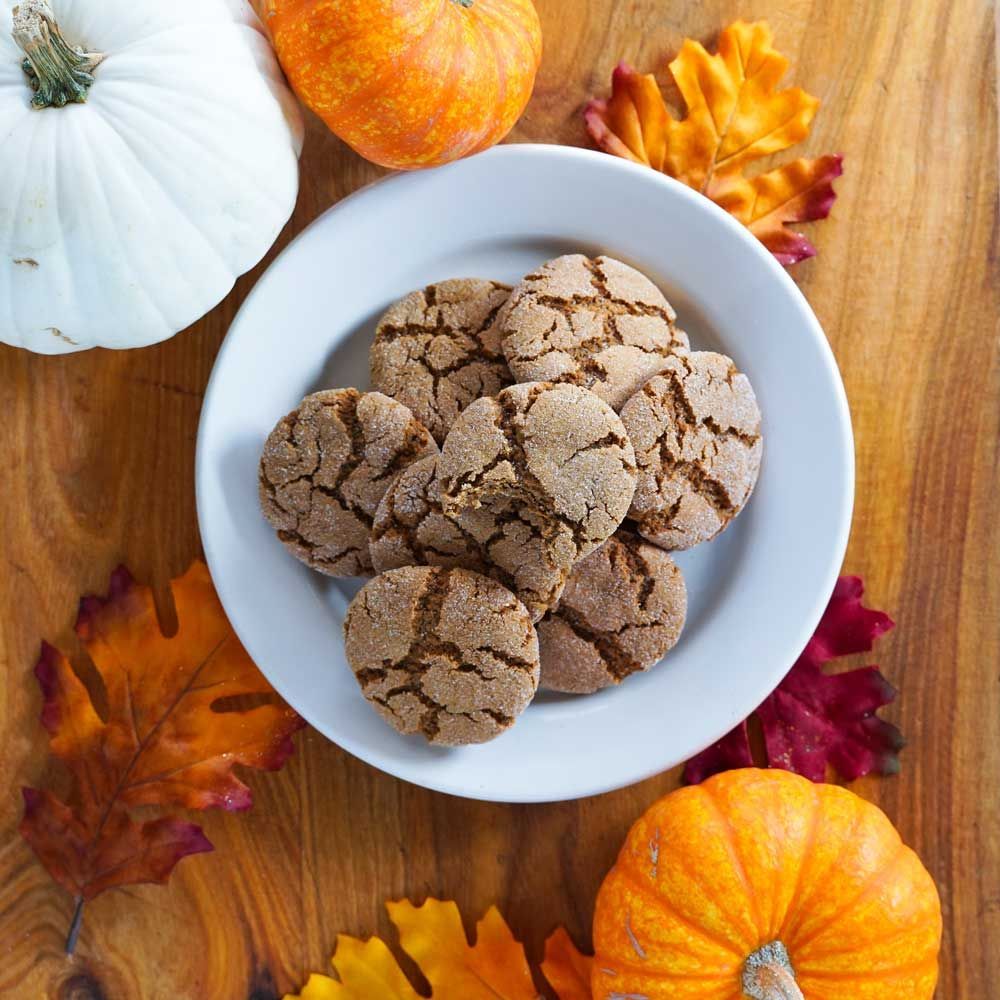 A plate of cookies surrounded by pumpkins and leaves