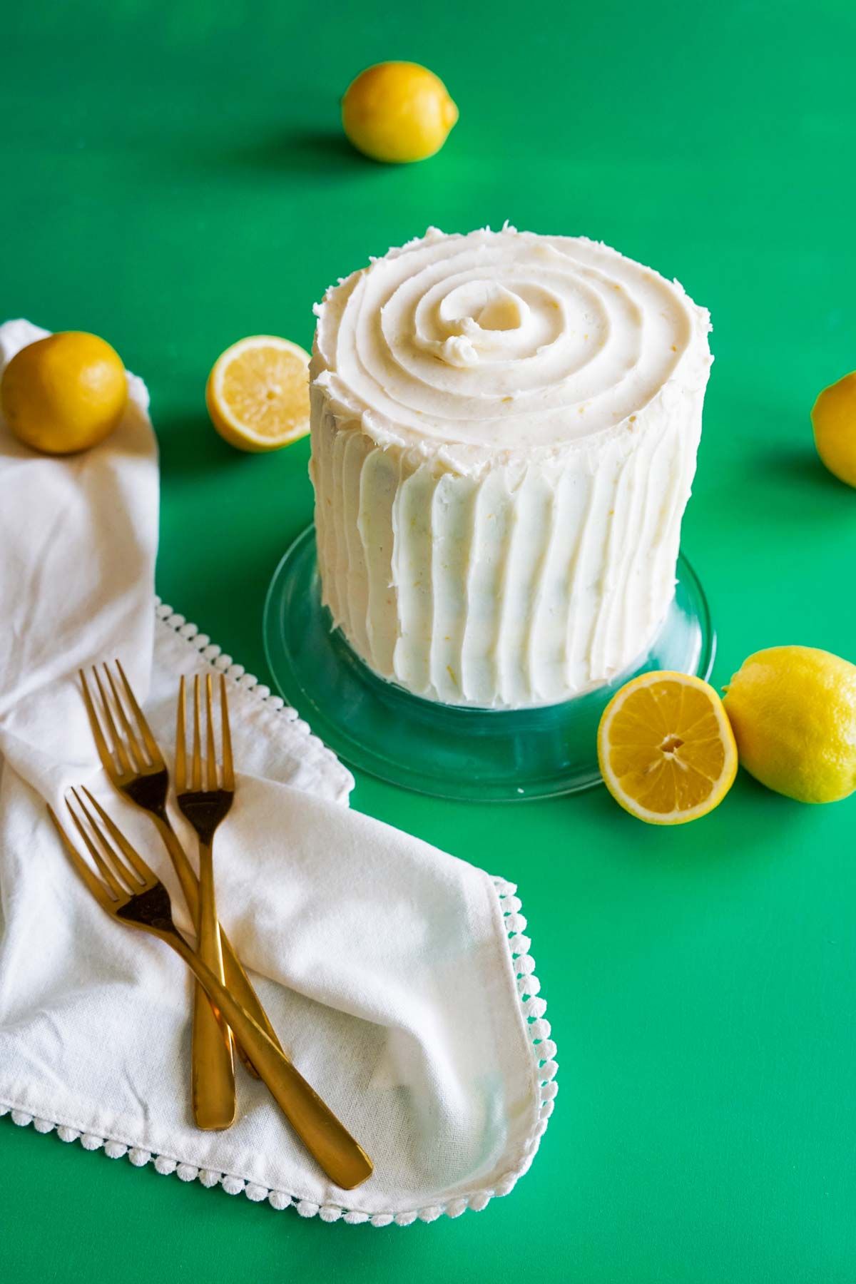 A cake with white frosting and lemons on a green table.