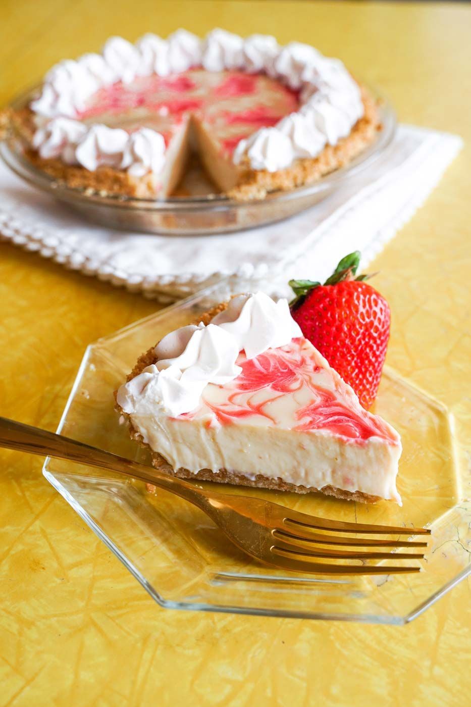 A slice of pie with whipped cream and a strawberry on a plate with a fork.