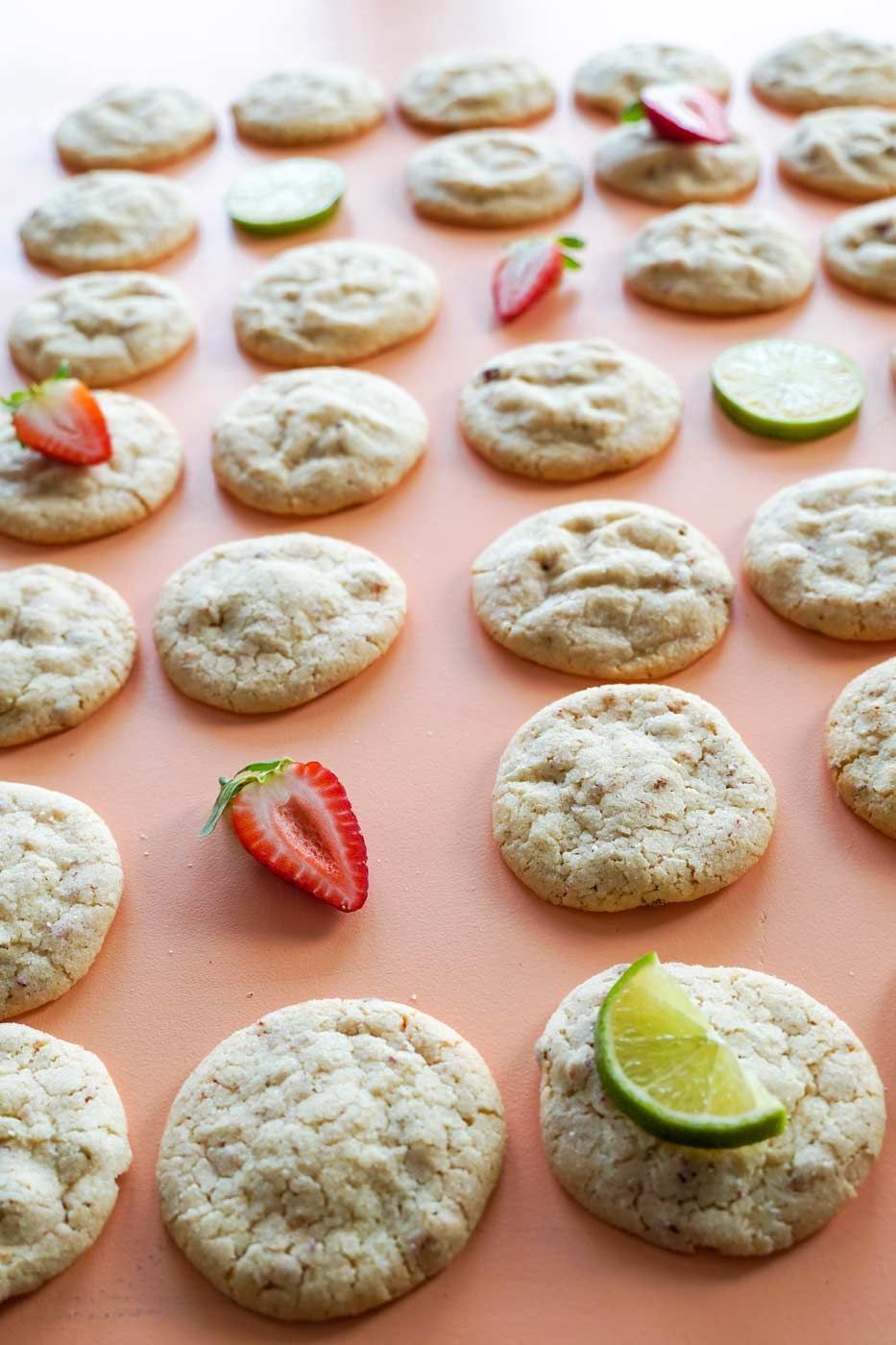 A bunch of cookies with strawberries and limes on them on a table.