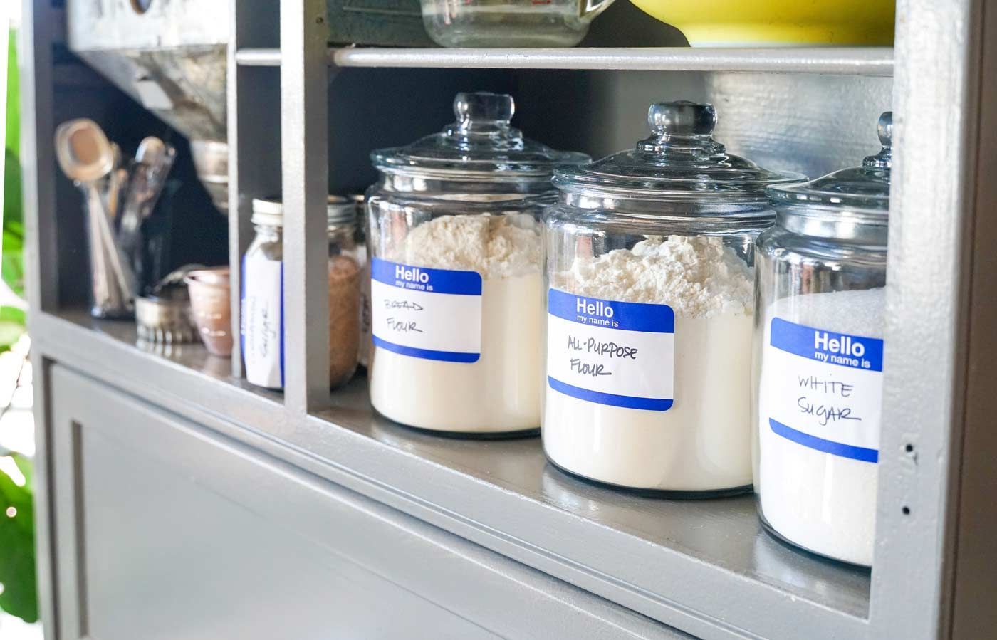 Three jars of flour are lined up on a shelf.