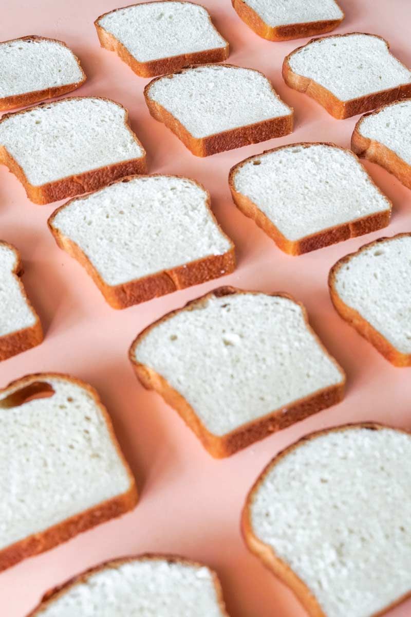 A bunch of slices of white bread on a pink surface.