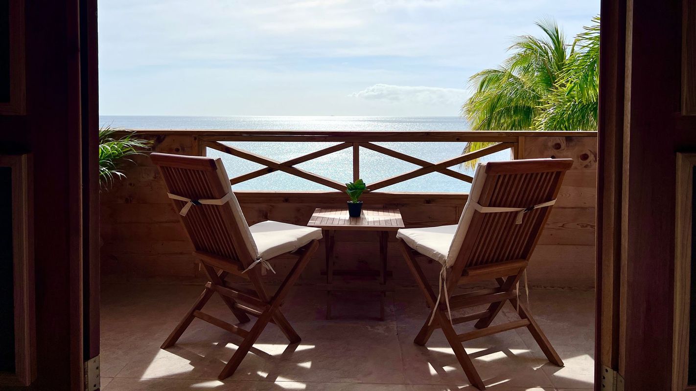 A balcony with two chairs and a table overlooking the ocean.