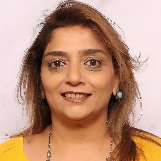 A woman is sitting at a desk with a laptop and a vase of flowers.